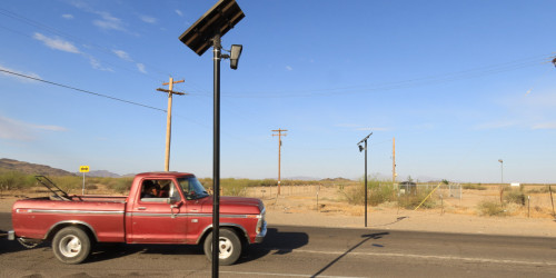 Flock Safety cameras A red truck carrying a lawnmower passes two Flock Safety ALPRs attached to poles.